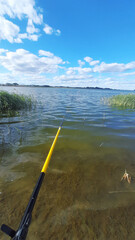 Fishing on a tranquil lake with a clear blue sky and gentle waves in the background during a sunny...