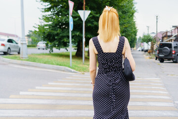 Woman in polka dot dress crossing street in a quiet neighborhood on a sunny day with green trees