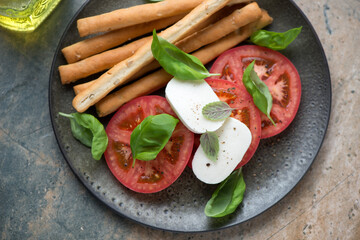 Olive-colored plate with italian caprese and grissini, horizontal shot on a beige and grey granite...