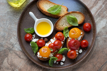 Bruschettas with roasted mixed tomatoes, ricotta and green basil on a brown plate, horizontal shot,...