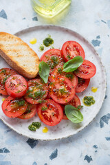 Plate with sliced red tomatoes, basil oil and ciabatta on a white and blue granite background, vertical shot, middle close-up