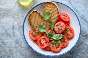 Tomato salad with basil oil, green basil and grilled ciabatta in a white and blue plate, horizontal shot, high angle view