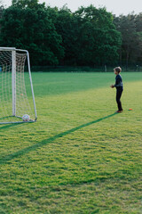 Boy is standing on a soccer field with a soccer ball in front of him