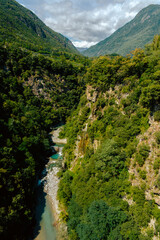 Small waterfall and turquoise river flowing through rocky valley with green vegetation in Sondrio,...