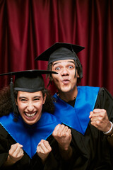 Portrait of two excited young adult multiethnic graduates celebrating achievement in photo booth,...