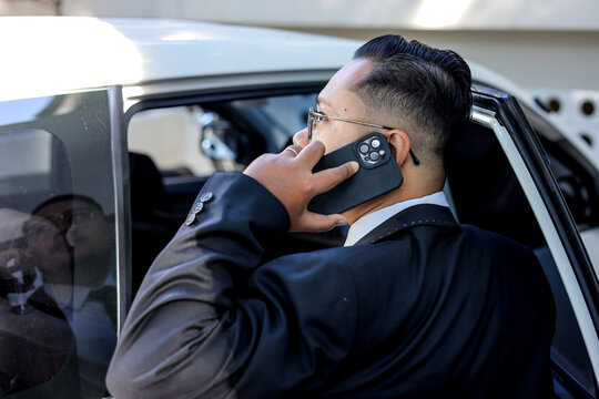 Businessman Talking On Phone While Entering Car Wearing Formal Suit - Powered by Adobe
