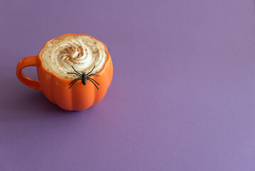 Halloween themed flat lay with a pumpkin latte and spiderwebs on a purple background.