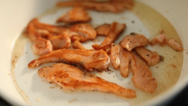 A woman cooks fresh salmon fillets in a skillet on her home kitchen stove, preparing a delicious and healthy meal for lunch.