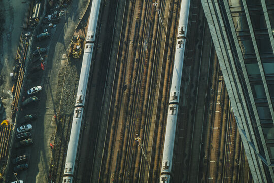 View of parallel trains stand on multiple tracks near parked cars and adjacent to a towering building, creating a dynamic urban scene, New York, New York, United States.