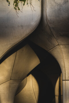View of a building with curved, metallic surfaces, a dance of light and shadow creating depth and intrigue, with subtle greenery above, New York, New York, United States.