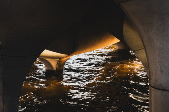 View of shimmering water reflecting golden light beneath the concrete arches, a stark contrast of textures and tones, creating a mesmerizing scene, New York, New York, United States.