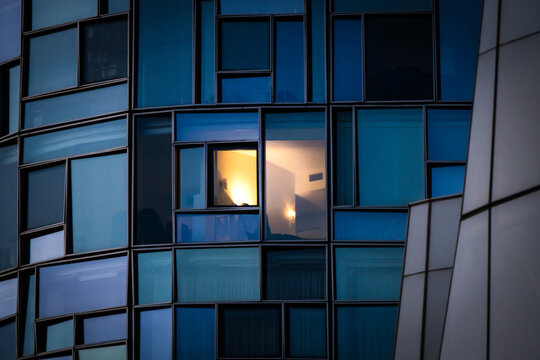 View of a modern building facade with geometric patterns of blue glass reflecting the city lights, contrasted by a single warmly lit window, New York, New York, United States.