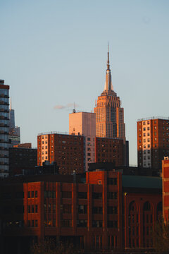 View of the majestic Empire State Building rising above the red brick buildings, bathed in the warm glow of the setting sun, New York, New York, United States.