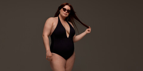 A plus-size woman exudes confidence in stylish swimwear and sunglasses against a neutral...
