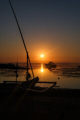 Radiant morning sun rises over Sanur Beach in Bali, illuminating the calm waters and traditional boats with a warm glow.