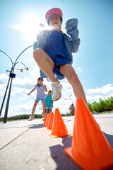 Kids maneuver around cones under a bright sky as part of outdoor activities, exhibiting agility and...