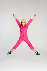 Trendy preteen girl joyfully jumps in pink overalls