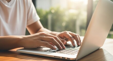 Person typing on a laptop computer with sunlight streaming through a window creating a warm atmosphere