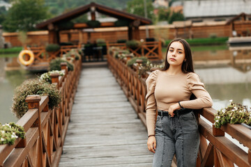A woman stands on a wooden bridge near a pond.