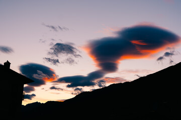 Pastel pink lenticular clouds drifting over mountain silhouette in serene evening sky