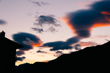 Pastel pink lenticular clouds drifting over mountain silhouette in serene evening sky