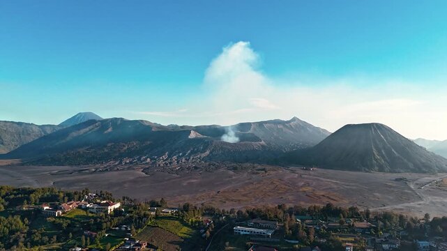 Forward-moving drone hyperlapse over Cemoro Lawang reveals steaming Mount Bromo with Mount Semeru on the horizon, sweeping across the Tengger caldera and the village at sunset