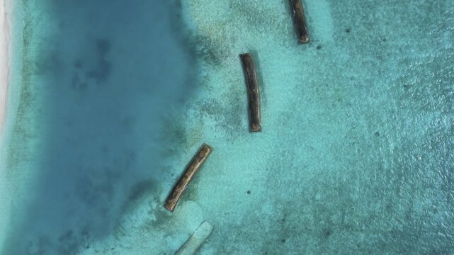 Aerial view of turquoise waters meeting the sandy shore, with dark structures breaking the surface, creating a striking contrast, Maldives, Maldives.