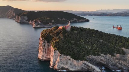 Aerial view of a lighthouse and buildings on a green cliff overlooking the blue sea with surrounding land, Portovenere, Liguria, Italy.