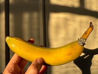 Landscape photo of an oval diamond engagement ring paired with a banana, lit by warm golden tones...