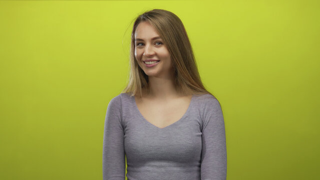 Young caucasian woman smiling over an isolated yellow background wall wearing a grey top, radiating positivity and confidence.