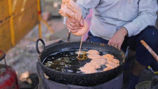 Street food jalebi being fried in a large pan as dough flows into sizzling oil, creating golden circular shapes of the traditional Indian sweet snack enjoyed at festivals and markets.
