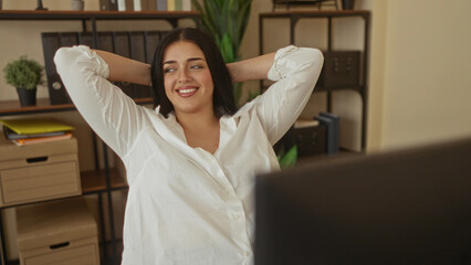 Woman lounging in modern office with relaxed expression surrounded by shelves and plants showcasing a comfortable workplace for business tasks.