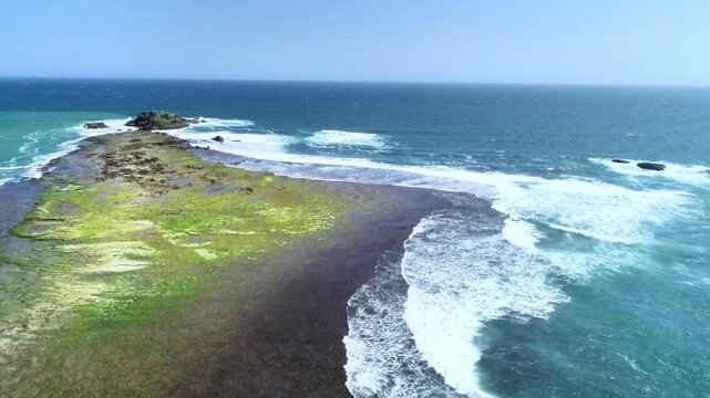 Drone aerial footage showing a small tropical island surrounded by turquoise sea, clear shallow water, and gentle waves under bright sunny weather. Perfect for travel, nature, and coastal landscape.