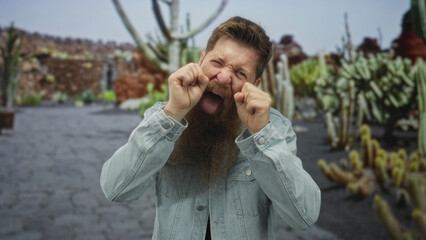 Man mimes crying with fists at eyes and scrunched face on street lined with cactus plants in park;...