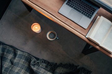 Cozy Work Corner: Overhead view of a warm-toned desk with a candle, book, coffee cup, and laptop