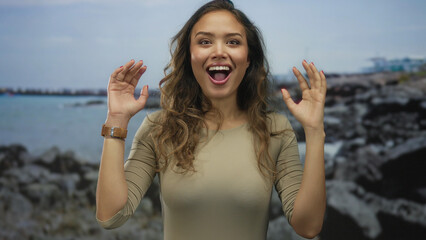 Woman with excited expression standing on a rocky seaside beach under a cloudy sky, exemplifying...