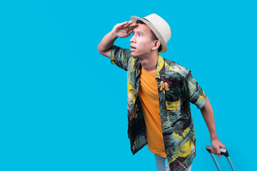 Young Indonesian Man Looking Into The Distance While Holding a Suit Case On A Blue Background