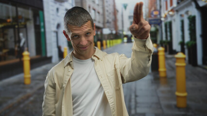 Man smiling outdoors on a vibrant city street gesturing with fingers on forehead, evoking a casual,...