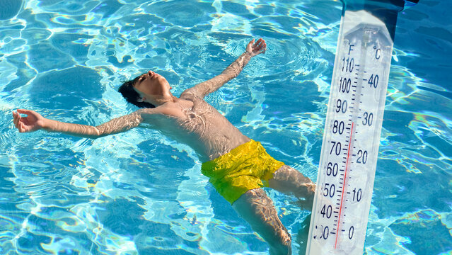 boy floating in a pool with a water thermometer on a hot day