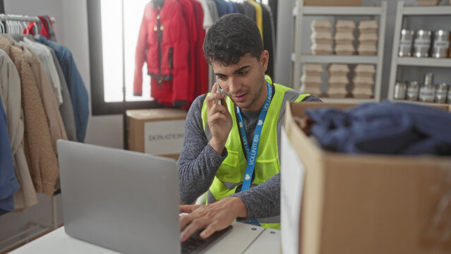 Man guides hands typing on laptop to coordinate volunteer donation drive with hispanic young crew during phone call.