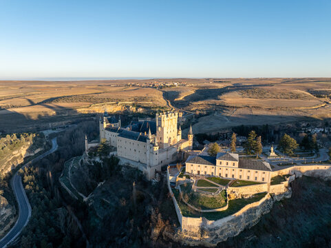 Aerial view of the Alc&Atilde;&iexcl;zar de Segovia, a majestic stone fortress perched atop a rocky crag, casting long shadows in the golden light, Segovia, Castilla y Le&Atilde;&sup3;n, Spain.