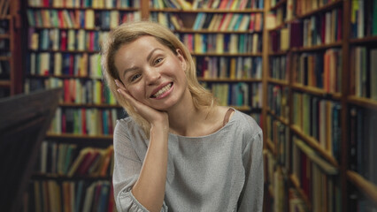 Woman with hand on chest in old library building surrounded by bookshelves and stacked volumes;...