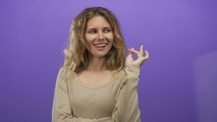 Woman holds hand gesture in studio with blonde young model against purple background while smiling...