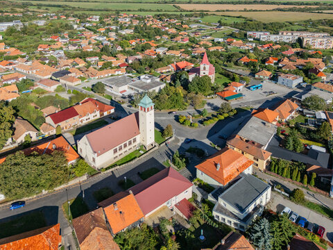 Aerial view of the town featuring red-roofed buildings and the church, a symphony of color against the green landscape, Pukanec, Nitra Region, Slovakia.
