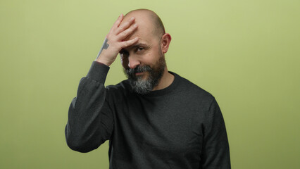 Bald man with beard and tattoo covers face on isolated yellow background conveying emotion