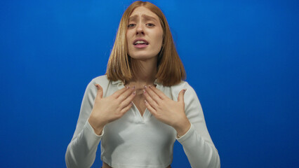 Young blonde woman waves bare hands enthusiastically in studio to signal someone over; invitation...