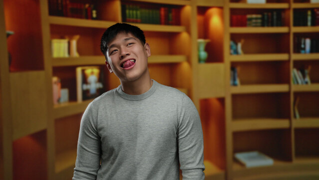 Young man in library with shelves in the background displaying a playful expression in an indoor room setting, showcasing a contemporary casual style.