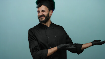 Hispanic chef in black uniform and gloves presenting with open hands against a blue background,...