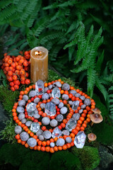 Burning candle, quartz crystal minerals and spiral made of snail shells and rowan berries in forest. Wiccan spiritual esoteric Magic ritual, Witchcraft. protective rowanberry ceremony