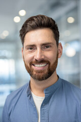 A cheerful man smiles warmly in a bright, modern office setting. Natural light enhances the...